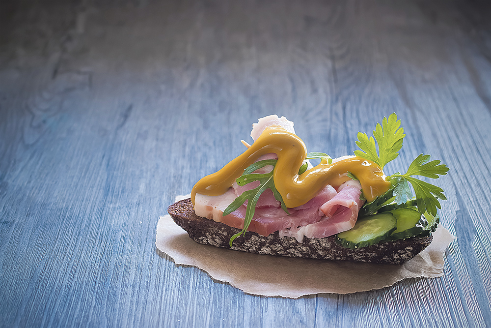 Sandwich with ham, fresh cucumber and mustard on brown paper.